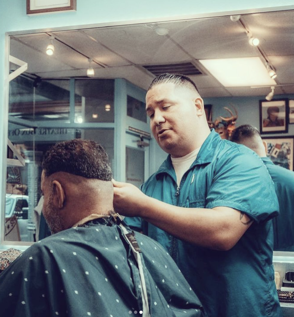 Ben, in a teal barber jacket, carefully lining up a client's neckline